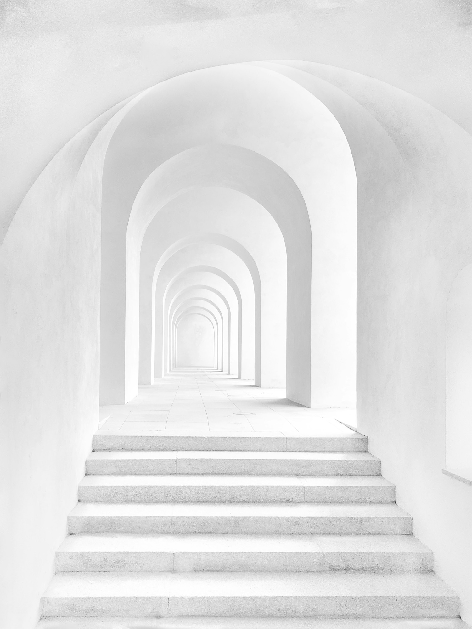 A long, arched white corridor and steps receding into soft daylight