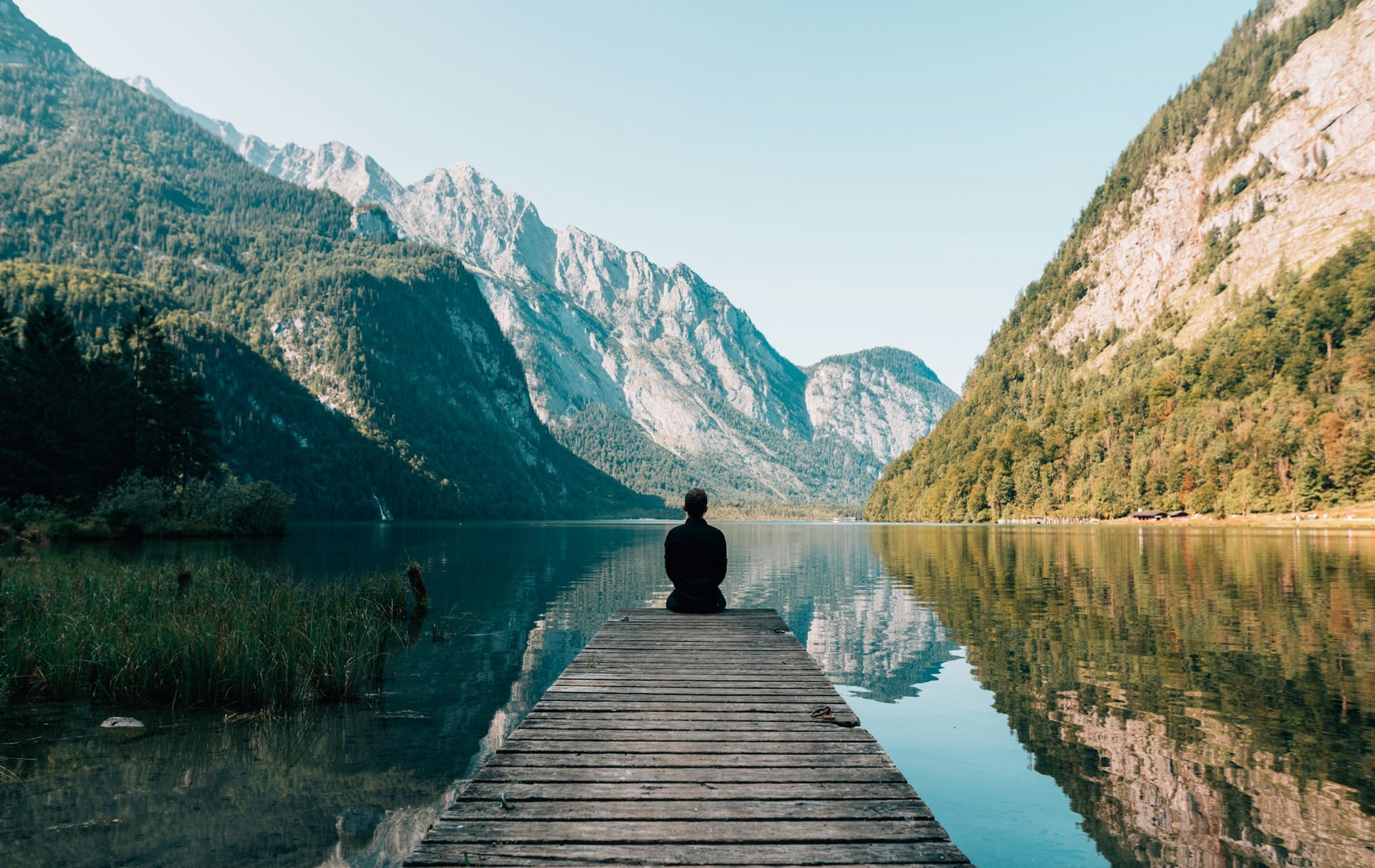 A still mountain lake at first light, with a wooden jetty reaching out toward distant peaks